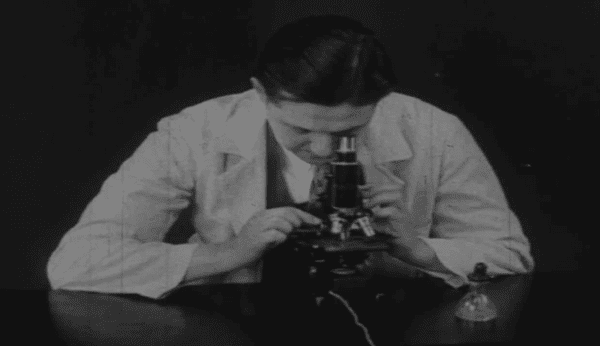 Black and white image of a scientist looking into a microscope